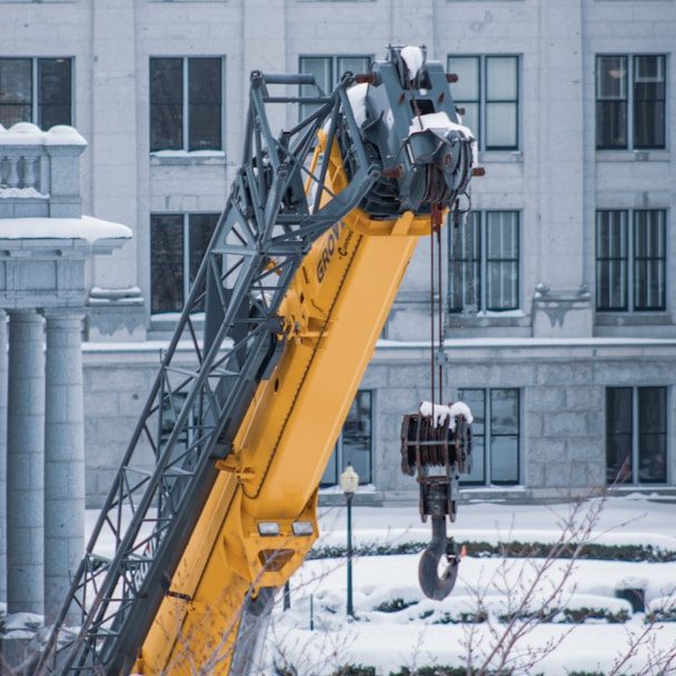 Grue jaune en plein hiver, avec neige sur les bâtiments environnants.
